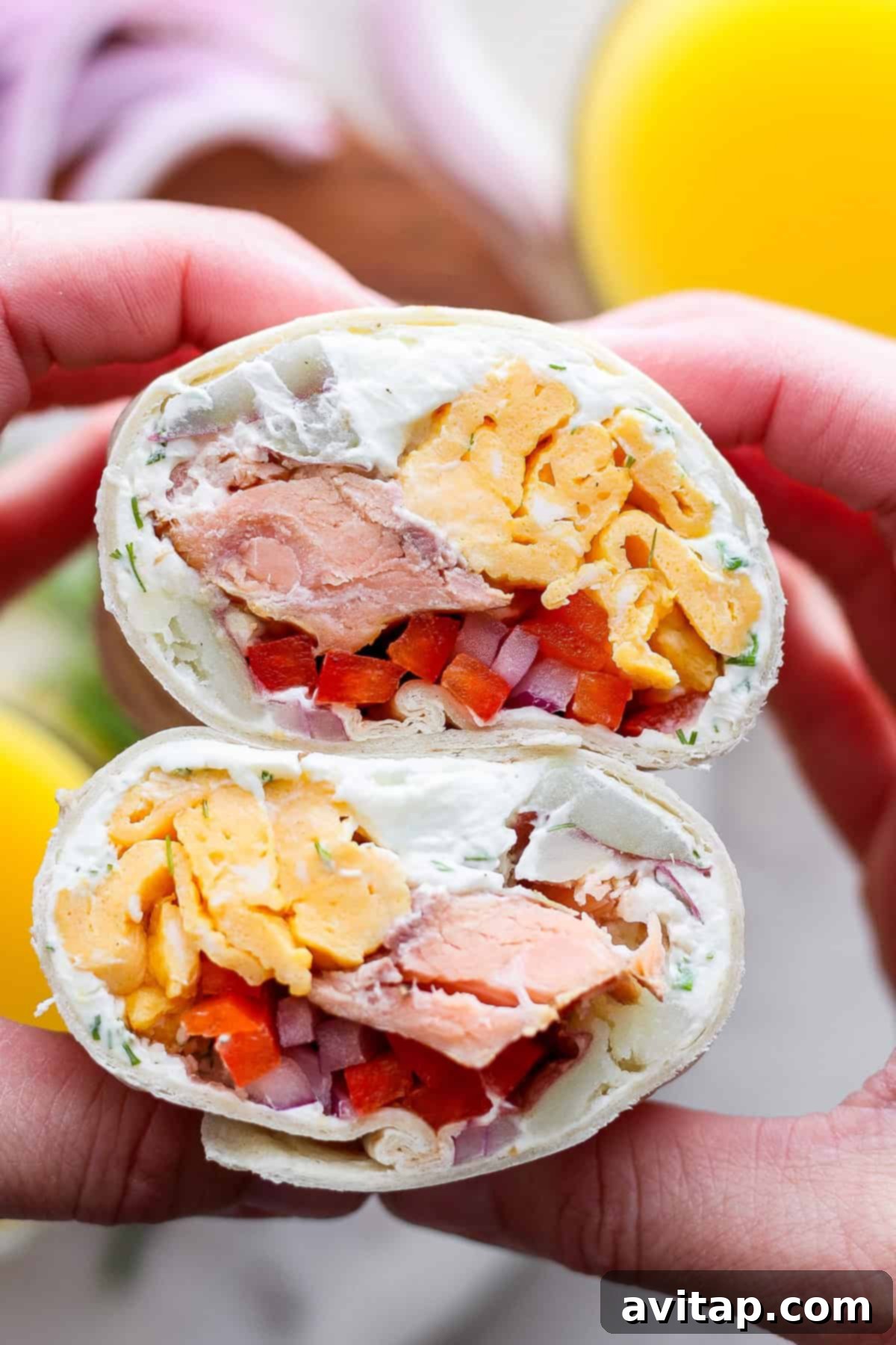 Close-up of a hand holding a halved wrap filled with salmon, cream cheese, diced vegetables, and scrambled eggs, showing the rich layers of filling.