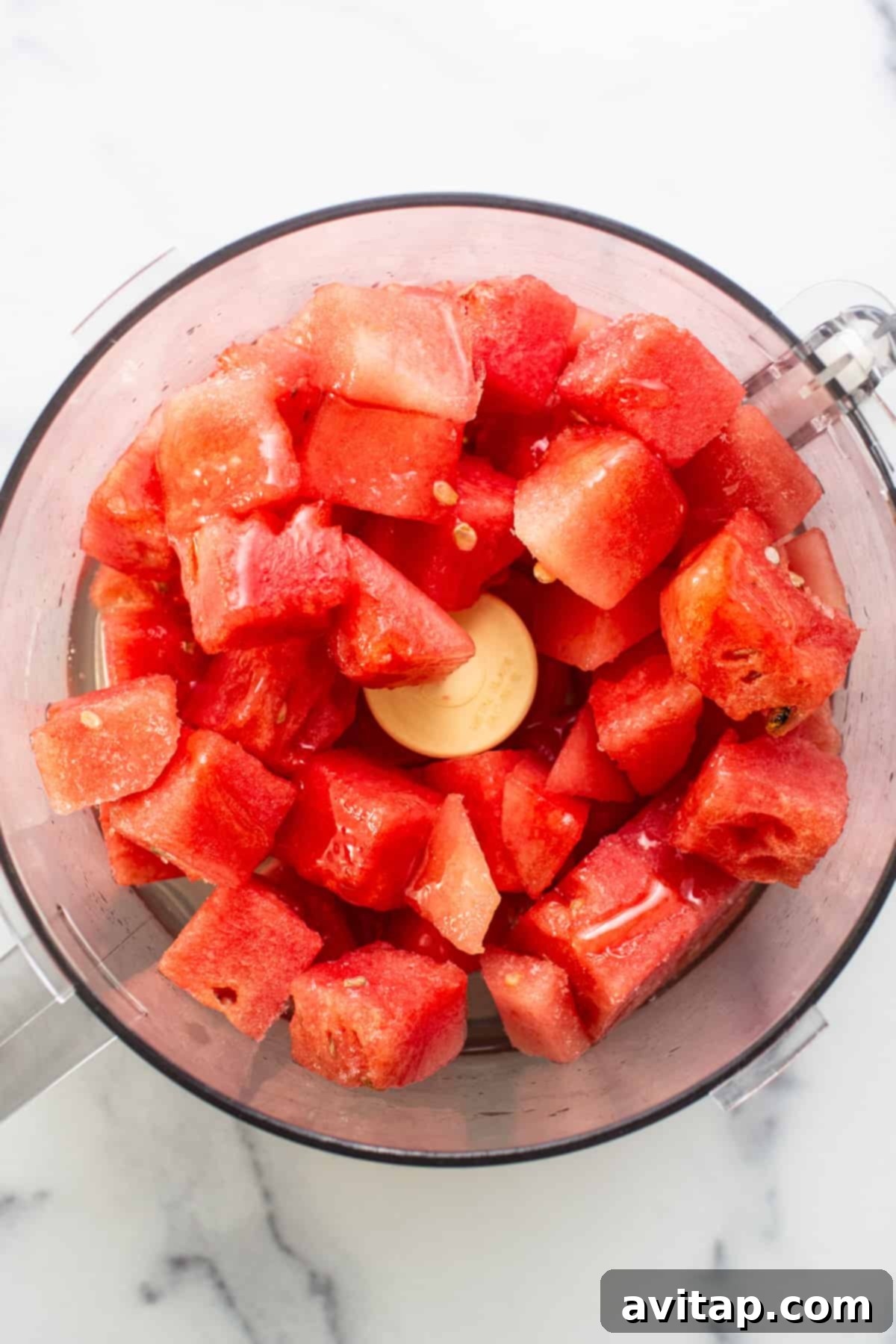 Close-up view of chunks of vibrant red watermelon, perfectly diced and ready to be processed, filling the base of a high-speed food processor bowl, anticipating its transformation into a smooth sorbet.