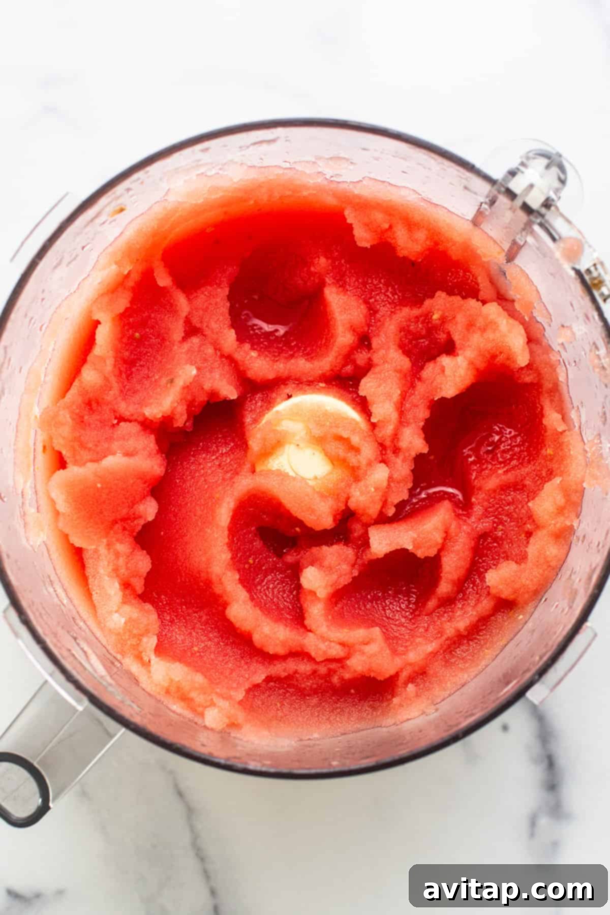 Dynamic top-down shot of a high-speed blender actively processing watermelon chunks, revealing a swirling vortex of vibrant red, indicating the powerful blending action transforming the fruit into a smooth mixture.