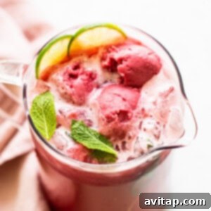 A large, inviting pitcher filled with a vibrant raspberry vodka punch, garnished with fresh mint and berries, ready to be served over sorbet, promising a refreshing summer cocktail.