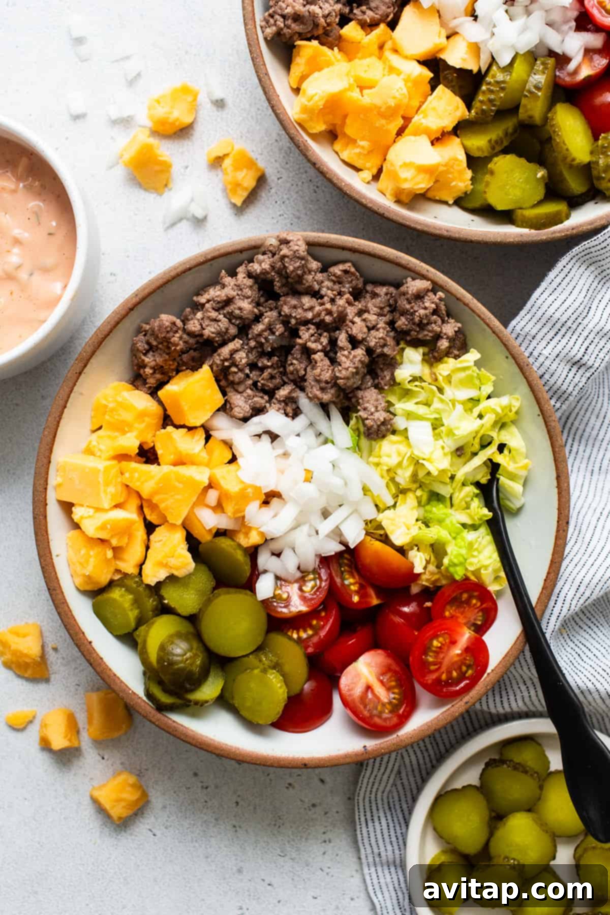 A vibrant salad bowl with distinct sections of ground beef, chopped tomatoes, onions, shredded cheese, crisp lettuce, and olives, accompanied by a side of creamy dressing for a customizable experience.