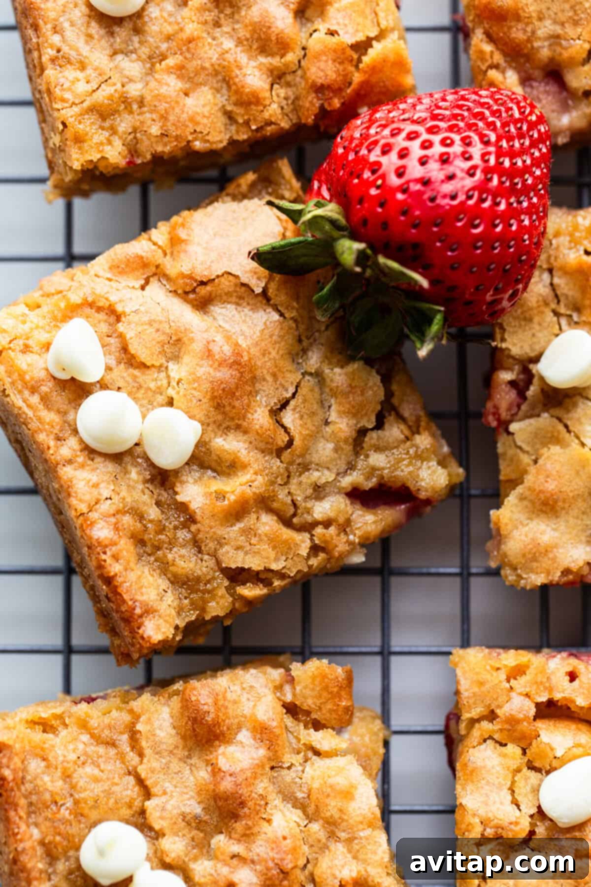Freshly baked strawberry blondies, showcasing melted white chocolate and vibrant strawberry pieces, cooling on a wire rack before being sliced into perfect squares.