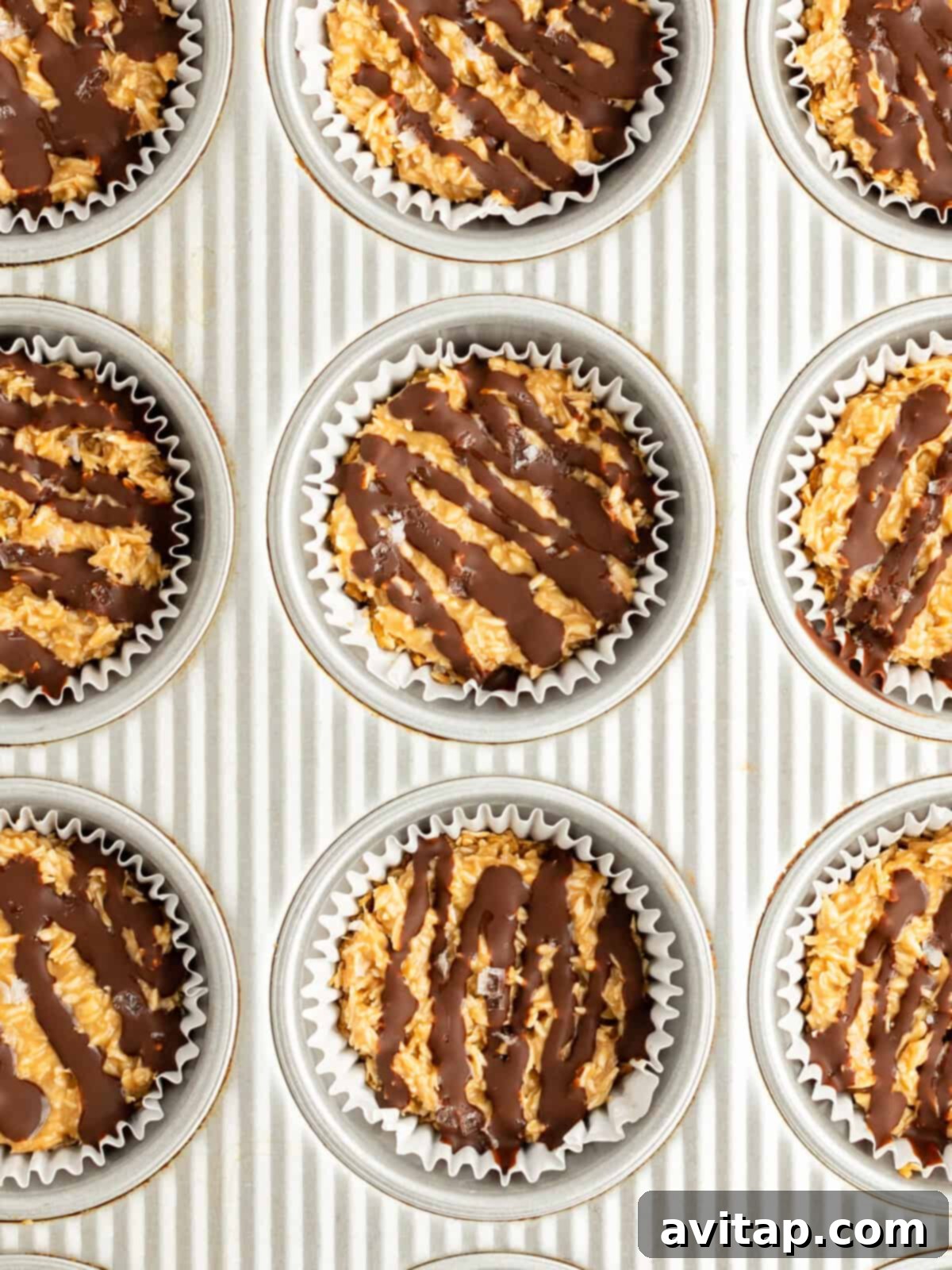 A baking sheet with nine muffin tin liners filled with a mixture topped with elegantly drizzled chocolate, showcasing the final touch.