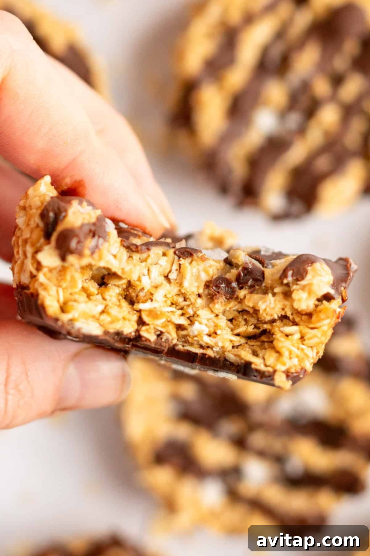 A hand holding a chocolate-drizzled oat bar with a bite taken out, revealing the delicious layers inside.
