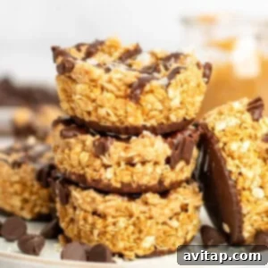 A stack of three granola clusters coated with chocolate. They are topped with flakes of salt and surrounded by chocolate chips.