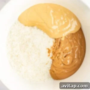 A bowl containing shredded coconut, smooth peanut butter, and crunchy peanut butter, prepared for the coconut layer.