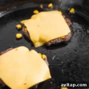 Two beef patties with melted cheese slices on top cooking in a skillet, showcasing the golden crust.