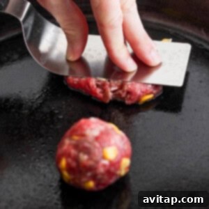 A person flattening a ball of ground meat on a skillet to form a patty, demonstrating the smash technique.