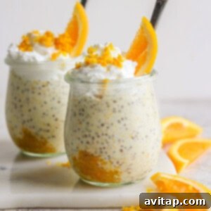 Sunshine Creamsicle Overnight Oats 10 Two glass jars filled with creamy creamsicle overnight oats, topped with whipped cream and orange slices, arranged on a white surface with additional orange wedges nearby.