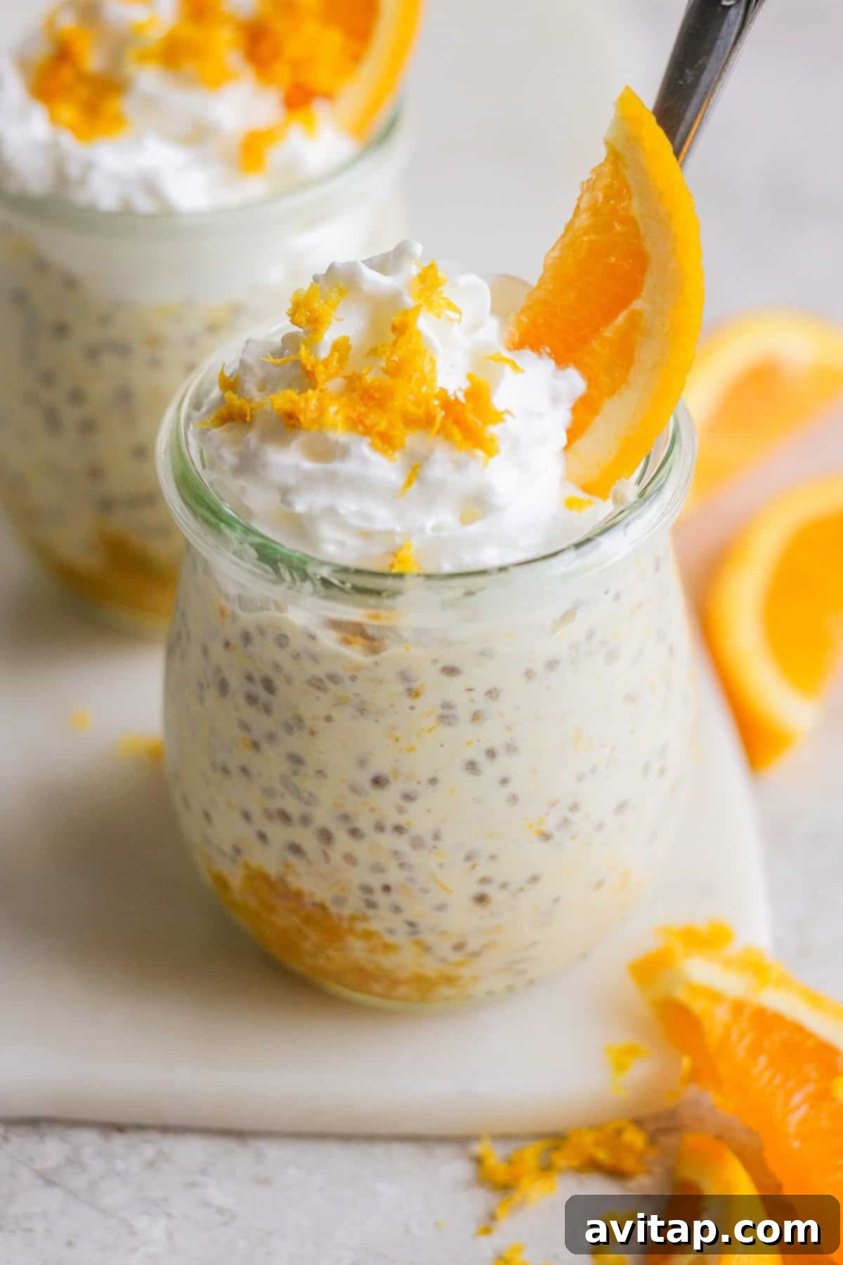 Sunshine Creamsicle Overnight Oats 5 Two small glass jars filled with creamy chia seed pudding, reminiscent of creamsicle overnight oats, are topped with whipped cream, orange zest, and an orange slice. Orange slices on the side complete this delightful treat.