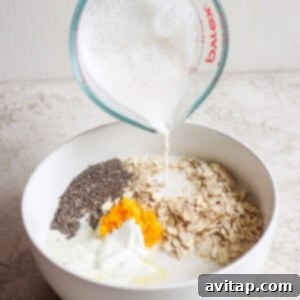 Sunshine Creamsicle Overnight Oats 8 A hand pours milk from a measuring cup into a white bowl containing oats, chia seeds, orange zest, and yogurt, creating the perfect base for creamsicle overnight oats.