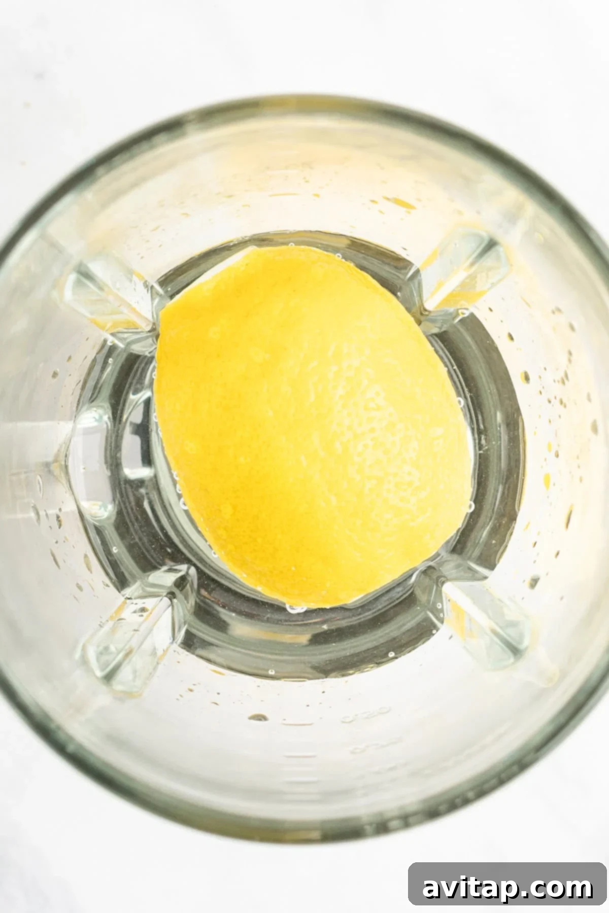 A halved lemon sits in a blender jar, viewed from above, ready to be blended.