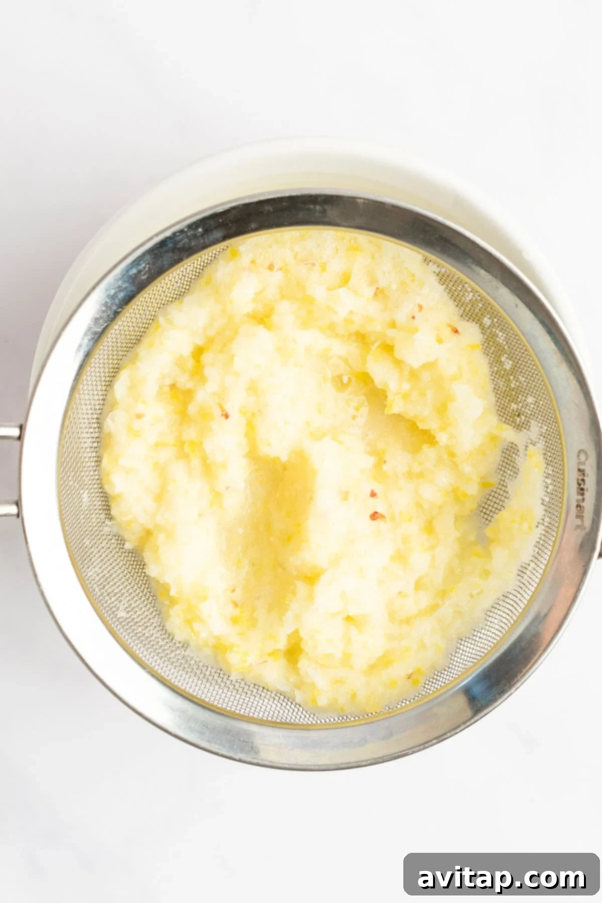 A metal sieve containing mashed potatoes over a white bowl.