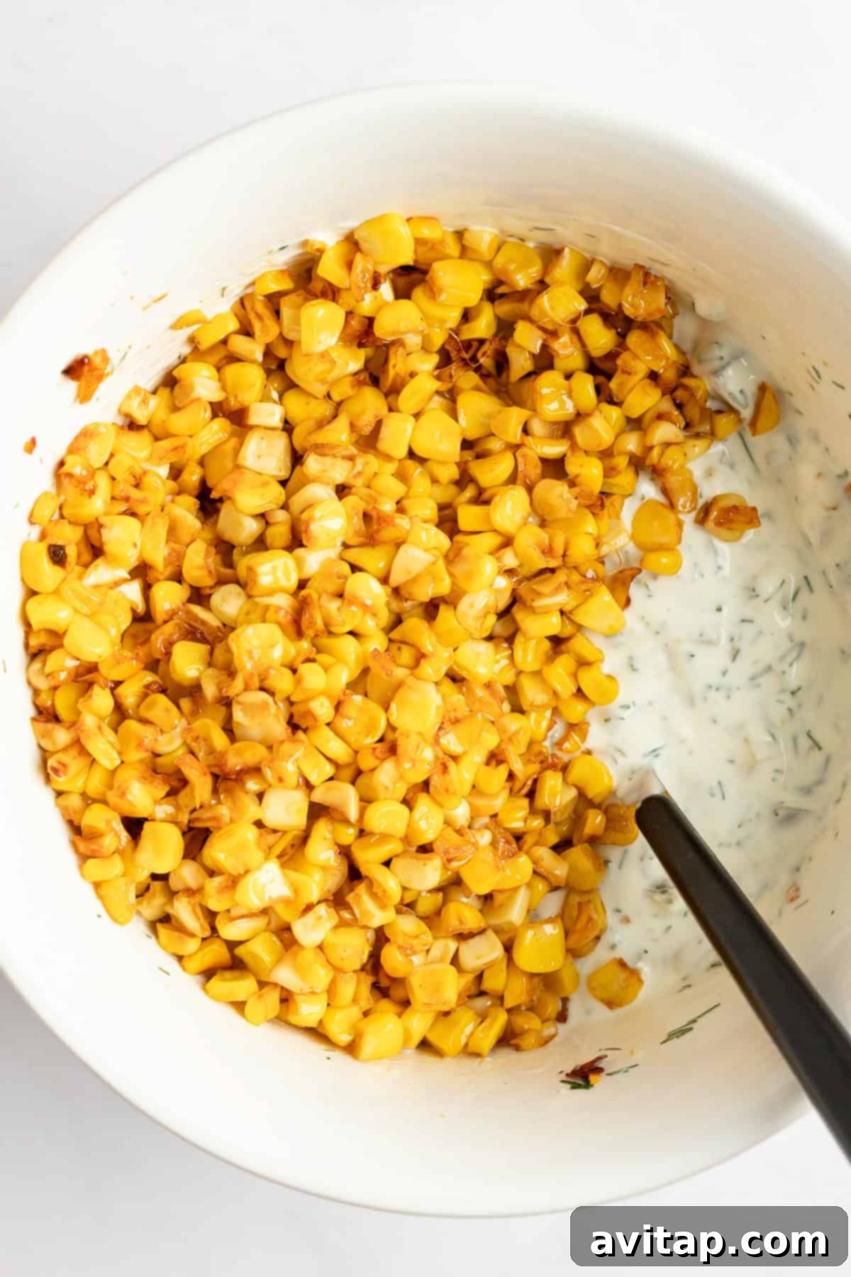 A bowl of roasted corn kernels mixed with a creamy, herb-infused dressing, and spoon partially immersed, showcasing the rich texture of the corn dill pickle dip.