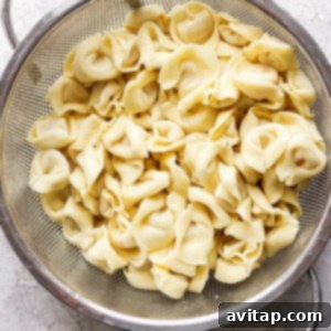 A metal colander filled with cooked cheese tortellini on a light-colored countertop.