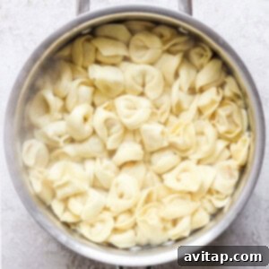 A pot filled with cooked cheese tortellini sitting on a light-colored surface.