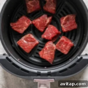 Effortless Air Fryer Steak Bites 11 Raw beef pieces arranged in an air fryer basket, ready for cooking.