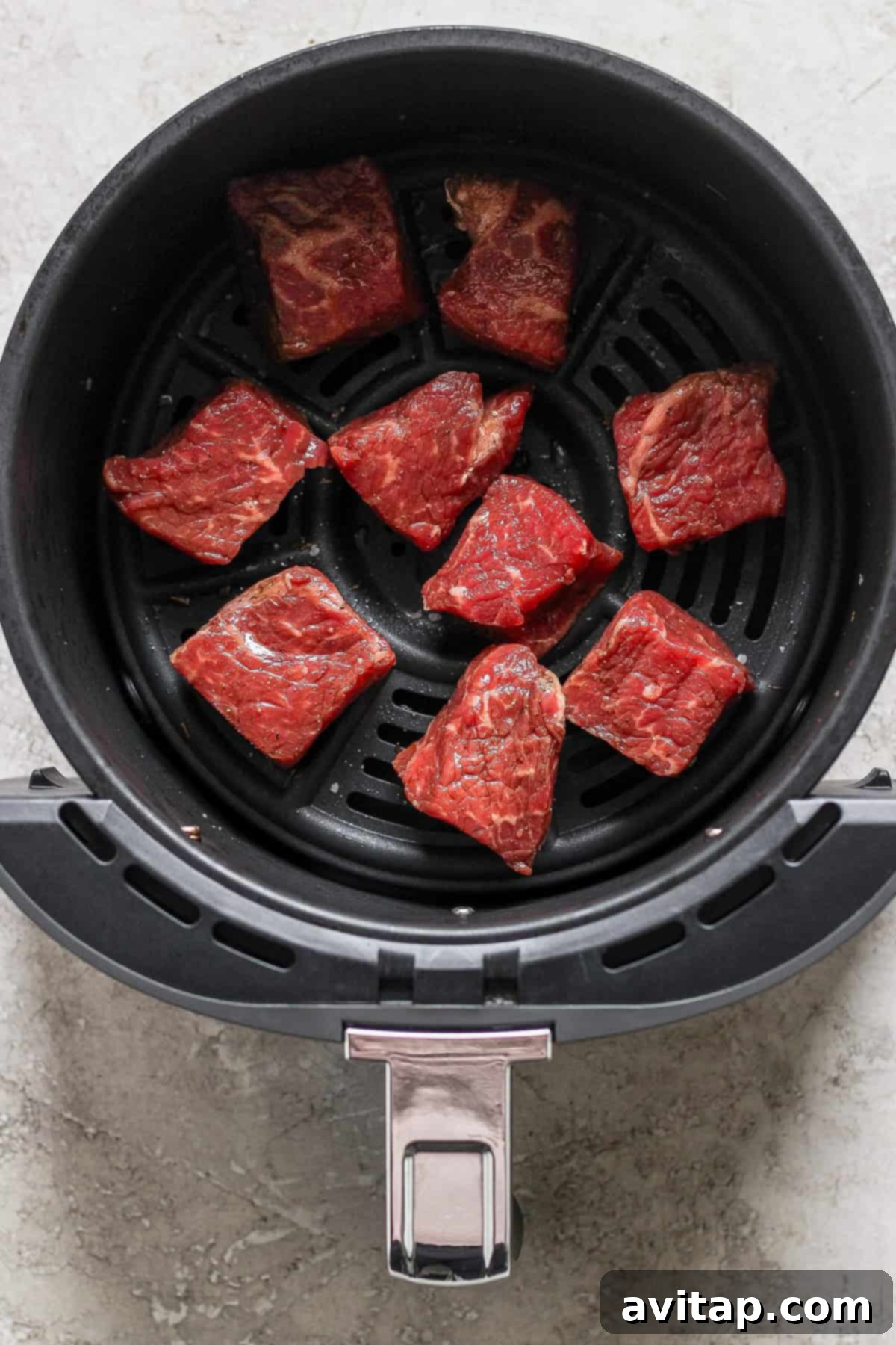 Effortless Air Fryer Steak Bites 3 An air fryer basket meticulously arranged with raw beef pieces, uniformly cut and ready for cooking, set against a light background.