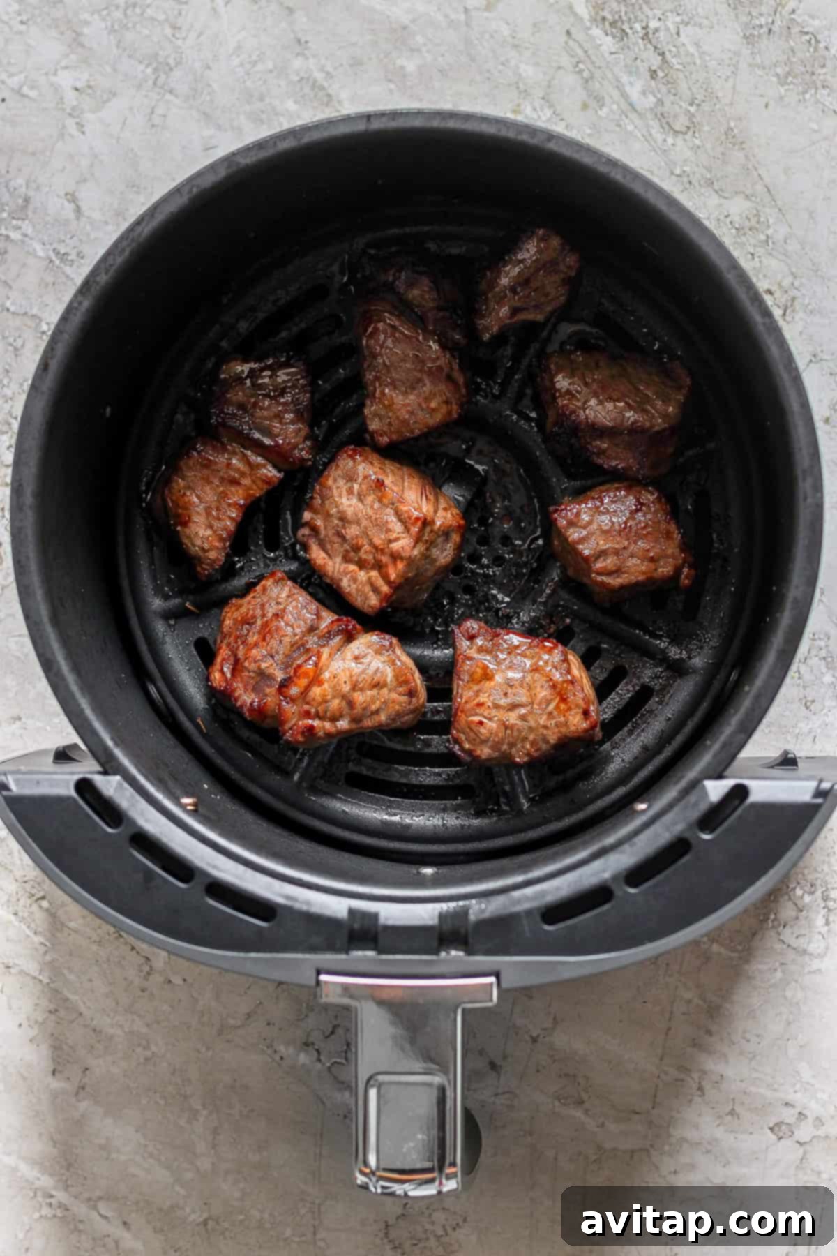 Effortless Air Fryer Steak Bites 5 Close-up of chunks of perfectly cooked, browned meat resting in an air fryer basket, showing a crispy exterior.
