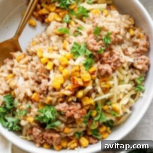 A bowl of risotto topped with ground meat, sweet corn, grated cheese, and chopped parsley with a gold-colored spoon on the side.