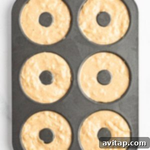 A six-cavity donut baking pan filled with unbaked donut batter, ready to be placed in the oven.