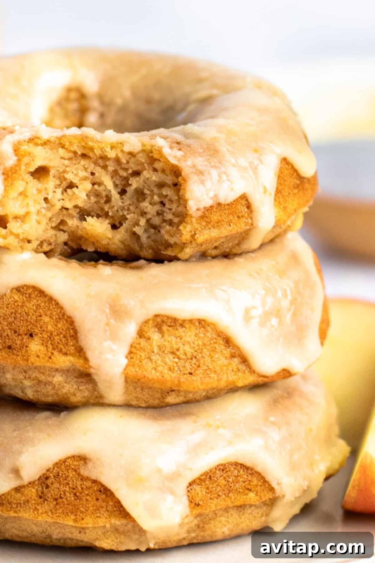 A stack of three glazed donuts with a bite taken out of the top one, showing their soft interiors.
