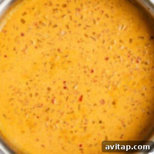 A metal pan filled with a bubbling, thick, orange-colored sauce containing small pieces of diced vegetables, simmering on a stovetop.