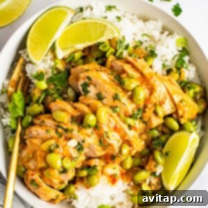 A bowl of white rice topped with sliced chicken, soybeans, and a creamy sauce, garnished with lime wedges and cilantro. Golden chopsticks rest beside the bowl. Lime slices are scattered around.