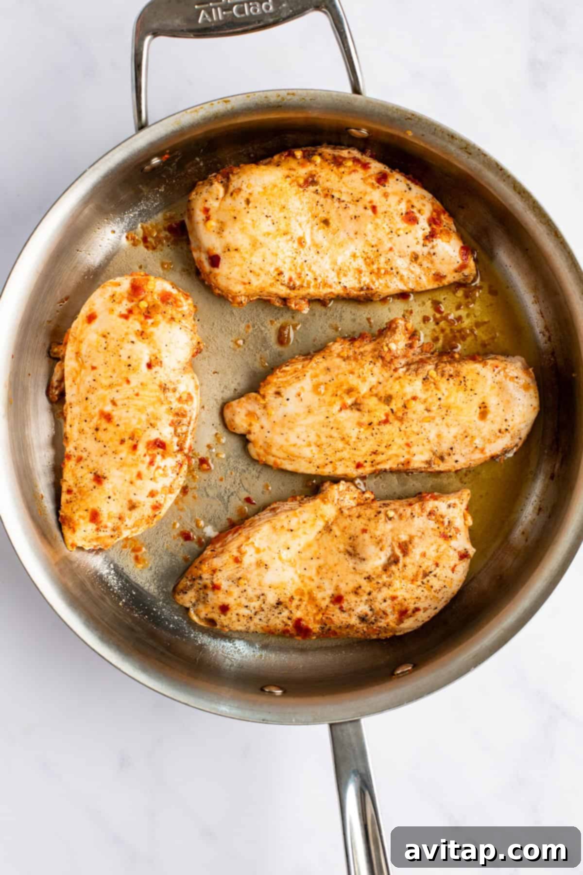 Four perfectly seasoned chicken breasts, golden brown and sizzling, cooking in a polished stainless steel skillet, ready to be incorporated into a delicious sauce.