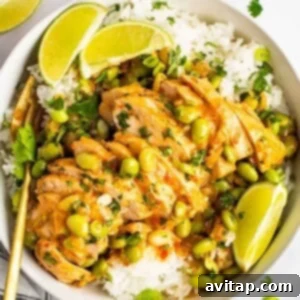 A bowl of skillet-cooked coconut chicken served over white rice, garnished with edamame beans, chopped herbs, and lime wedges.