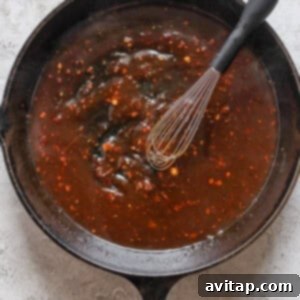 A black cast iron skillet filled with a dark brown sauce and a whisk resting inside.