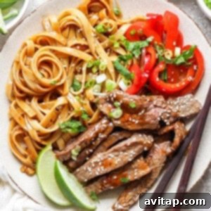 A plate with cooked noodles, sliced red bell peppers, and slices of beef topped with sesame seeds. A lime wedge is on the side, and a pair of chopsticks rests on the plate.