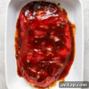 A raw marinated piece of meat lies in a white rectangular ceramic dish, coated with a reddish-brown sauce and garnished with herbs.