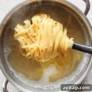 A pot of hot water with steam rising and cooked fettuccine noodles being lifted out using a spoon with slots.