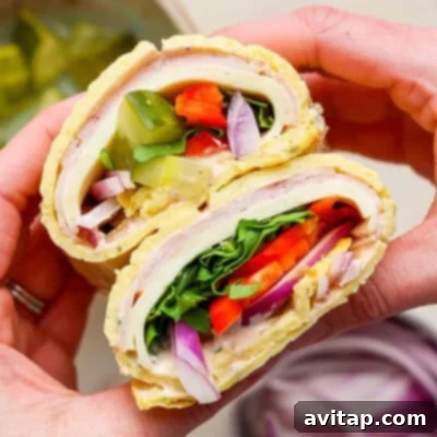Hands delicately holding a savory cottage cheese wrap, generously filled with slices of turkey, crisp lettuce, juicy tomato, tangy pickles, thinly sliced red onion, and fresh spinach, creating a perfect, healthy meal.