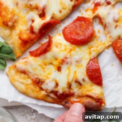 A hand confidently holds a delicious slice of pepperoni pizza, featuring perfectly melted cheese and crisp pepperoni, presented against a clean white parchment background.