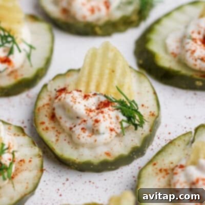 Crisp cucumber slices, elegantly topped with creamy sour cream, a crunchy potato chip, fresh dill, and a sprinkle of vibrant paprika, arranged on a pristine white surface for a delightful appetizer.