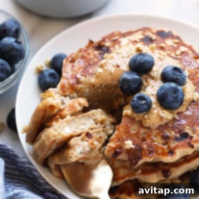 A stack of golden, protein-packed oatmeal pancakes, generously topped with fresh blueberries, served on a white plate, inviting a delicious and healthy start to the day.