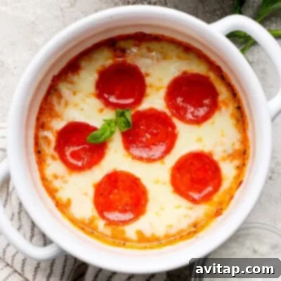 A perfectly baked dish, rich with melted cheese and six slices of savory pepperoni, artfully garnished with fresh basil, presented in a crisp white ceramic bowl on a textured surface.