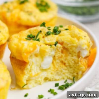 A baked egg muffin, with a tempting bite taken out revealing a fluffy interior and melted cheese, garnished with fresh chopped green onions on a simple white plate.