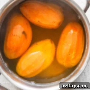 Four peeled sweet potatoes boiling in a stainless steel pot filled with water.