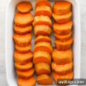 A white baking dish filled with sliced sweet potatoes arranged in three rows on a light surface.