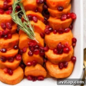 Sliced sweet potatoes topped with cranberries and garnished with a sprig of rosemary, served in a white dish.