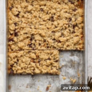 A metal baking pan filled with rustic, crumbly dessert bars. Two bars have been perfectly cut out, revealing a rich, layered filling. A charming fork and a napkin are artfully placed nearby, ready for serving.