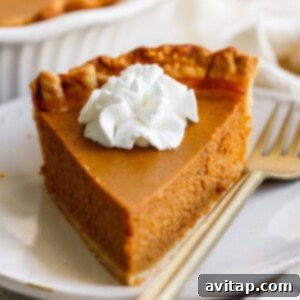 A slice of pumpkin pie topped with a dollop of whipped cream, placed on a white plate with a fork beside it.
