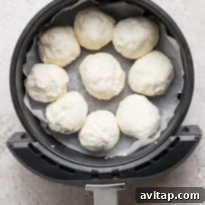 An air fryer basket, neatly lined with parchment paper, holds eight uncooked dough balls arranged in a circular formation, awaiting the egg wash.
