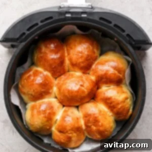 Golden brown homemade rolls, arranged in a circular pattern inside an air fryer basket, rest on a gray surface, cooling after baking.