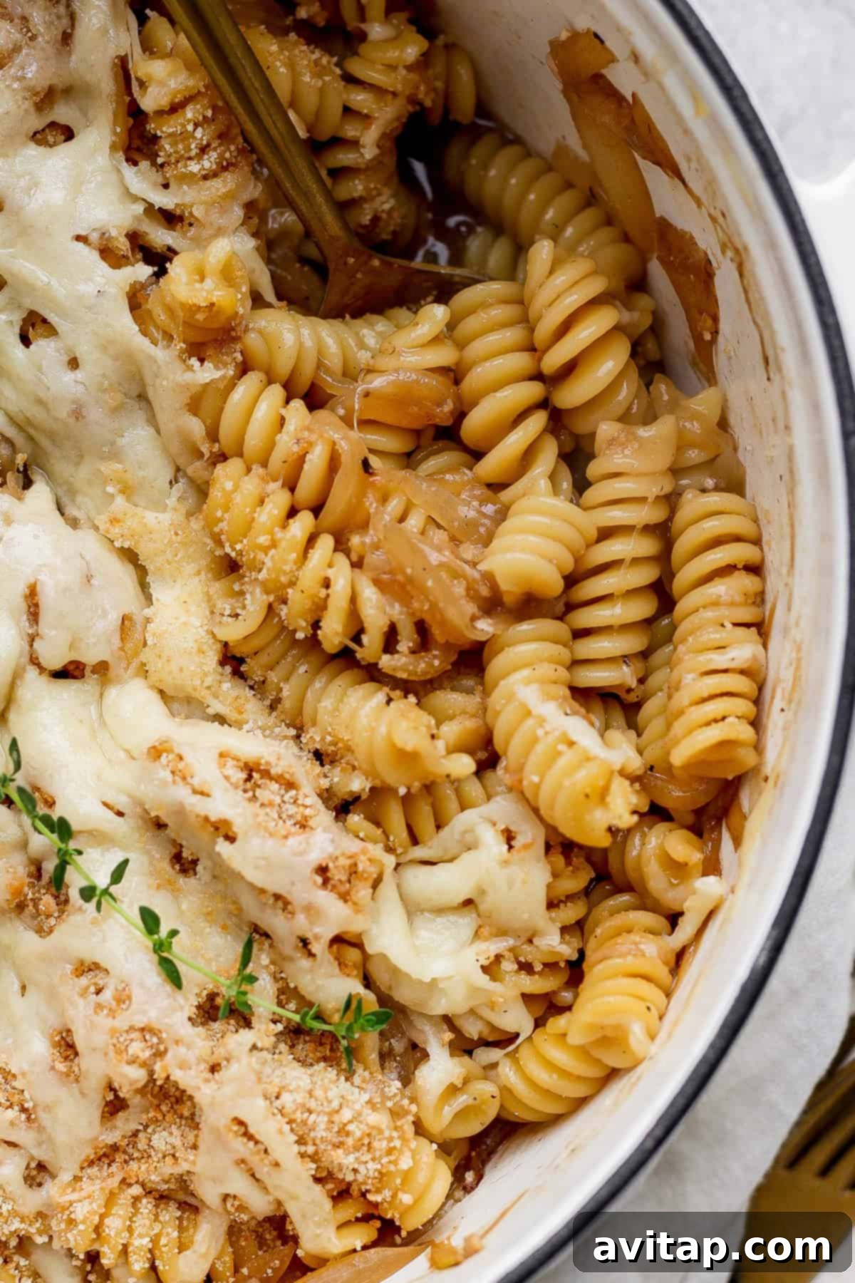 Sweet and Savory Onion Pasta 6 Close-up of baked rotini pasta with melted cheese, breadcrumbs, and herbs in a round dish. A fork is partially visible in the pasta.