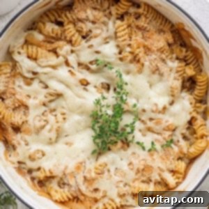A close-up of a baked pasta dish with spiral noodles topped with melted cheese, breadcrumbs, and a garnish of fresh herbs.