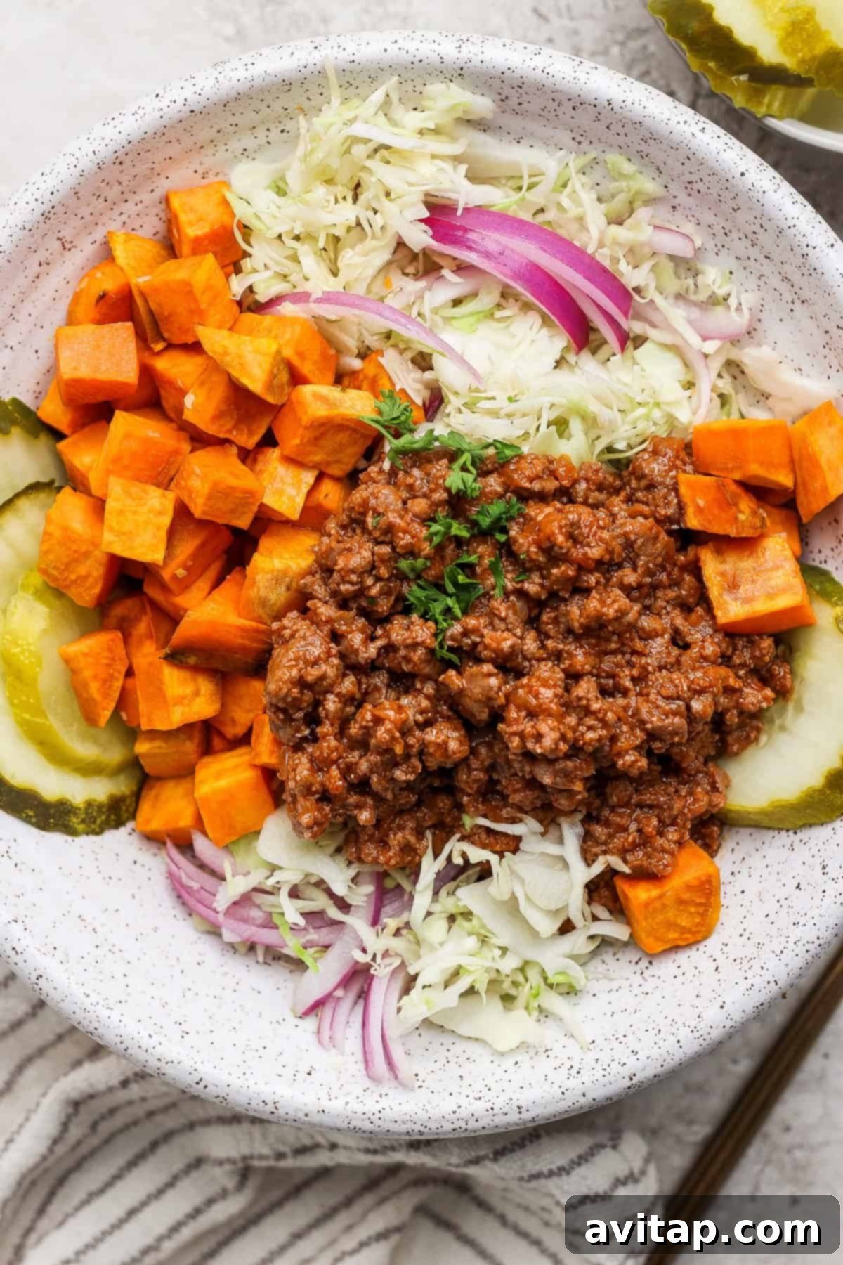 A vibrant Sloppy Joe Bowl featuring ground meat, perfectly roasted sweet potato cubes, tangy pickle slices, crisp shredded cabbage, and thinly sliced red onion.